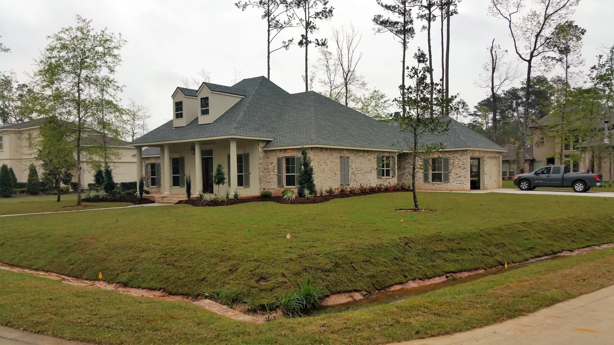 Completed brick and stucco home with a covered front entrance, garage and landscaped lawn.