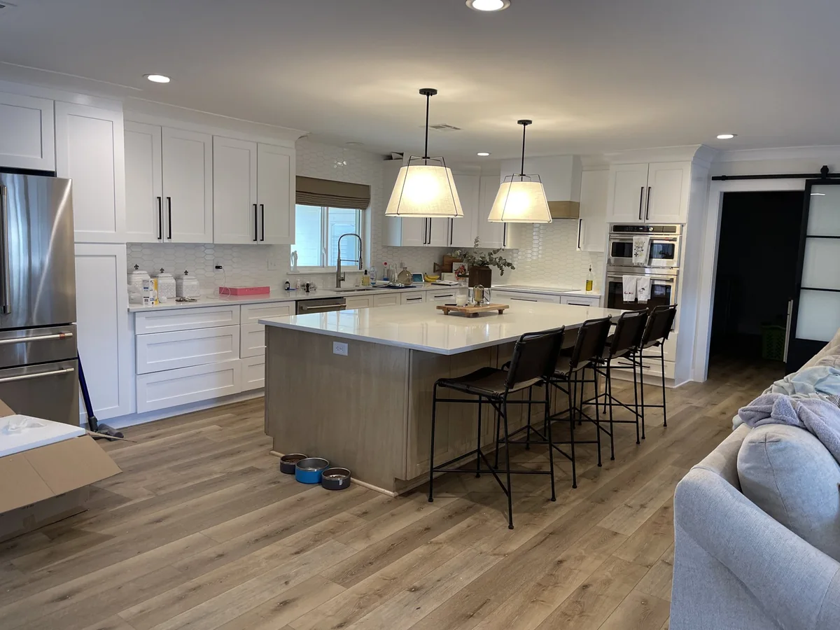 White kitchen with a wood island, pendant lights and seating opening into the living area