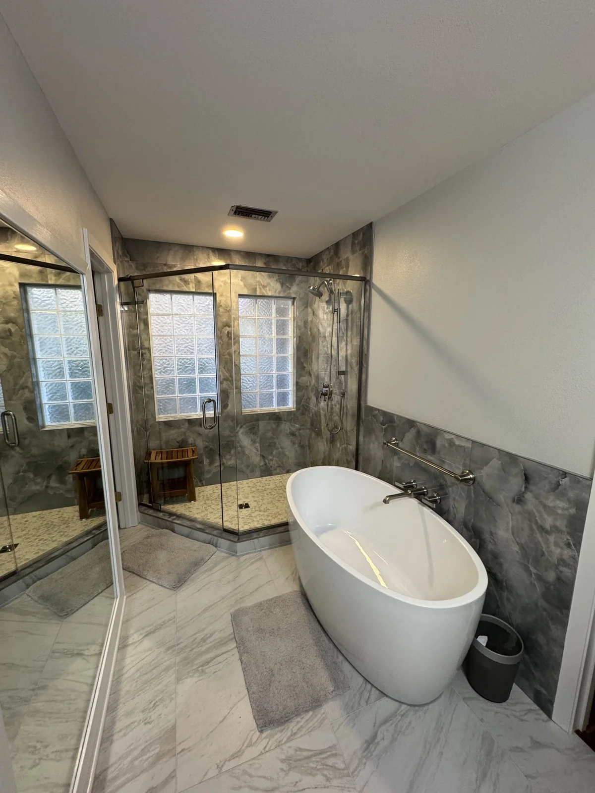 Freestanding white bathtub and glass shower with gray stone tile