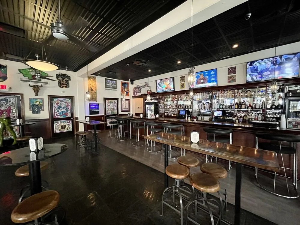 Bar interior with a long counter, wood tables and dark ceiling