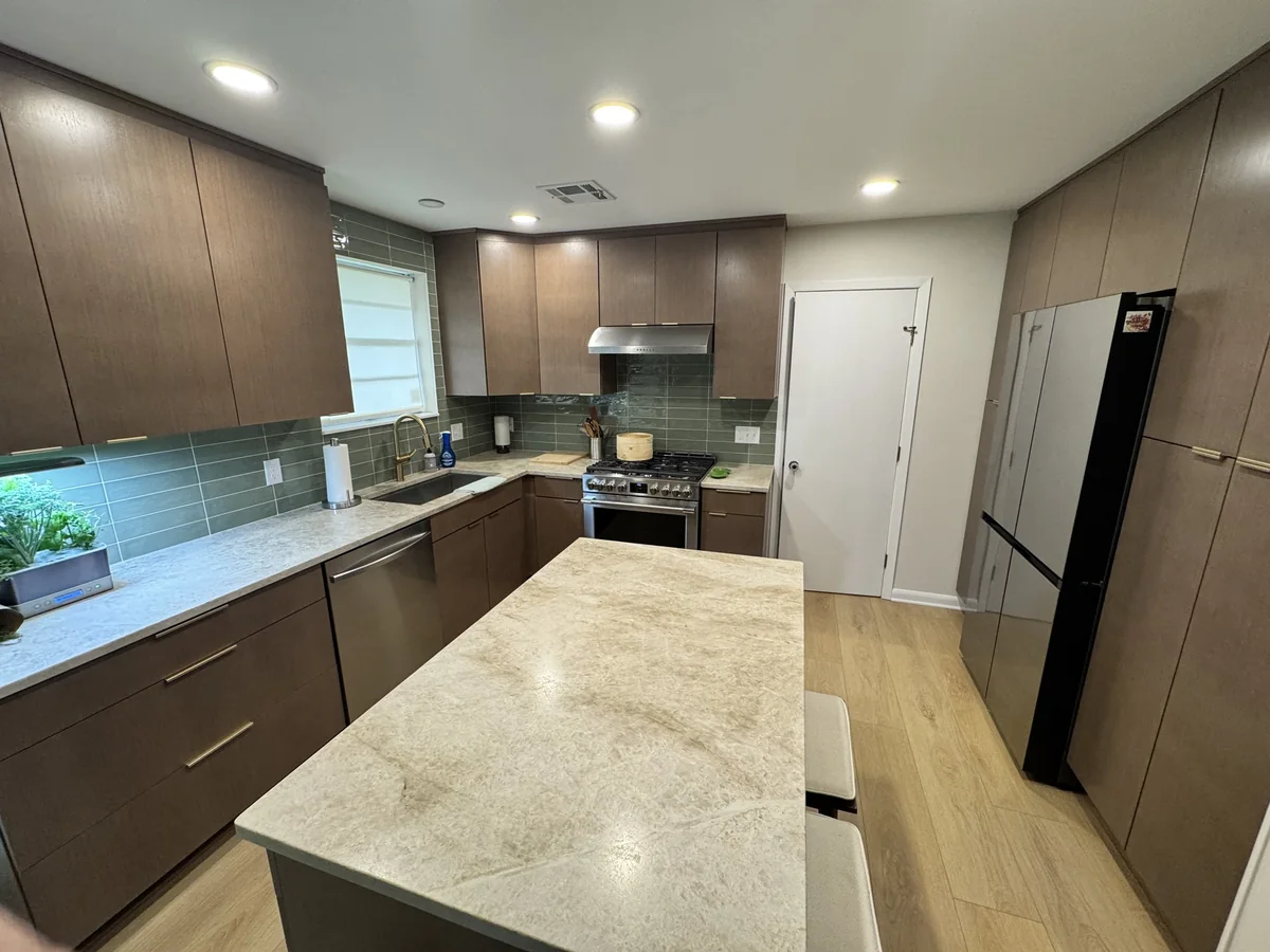 Kitchen with wood cabinetry, green tile backsplash and a stone island
