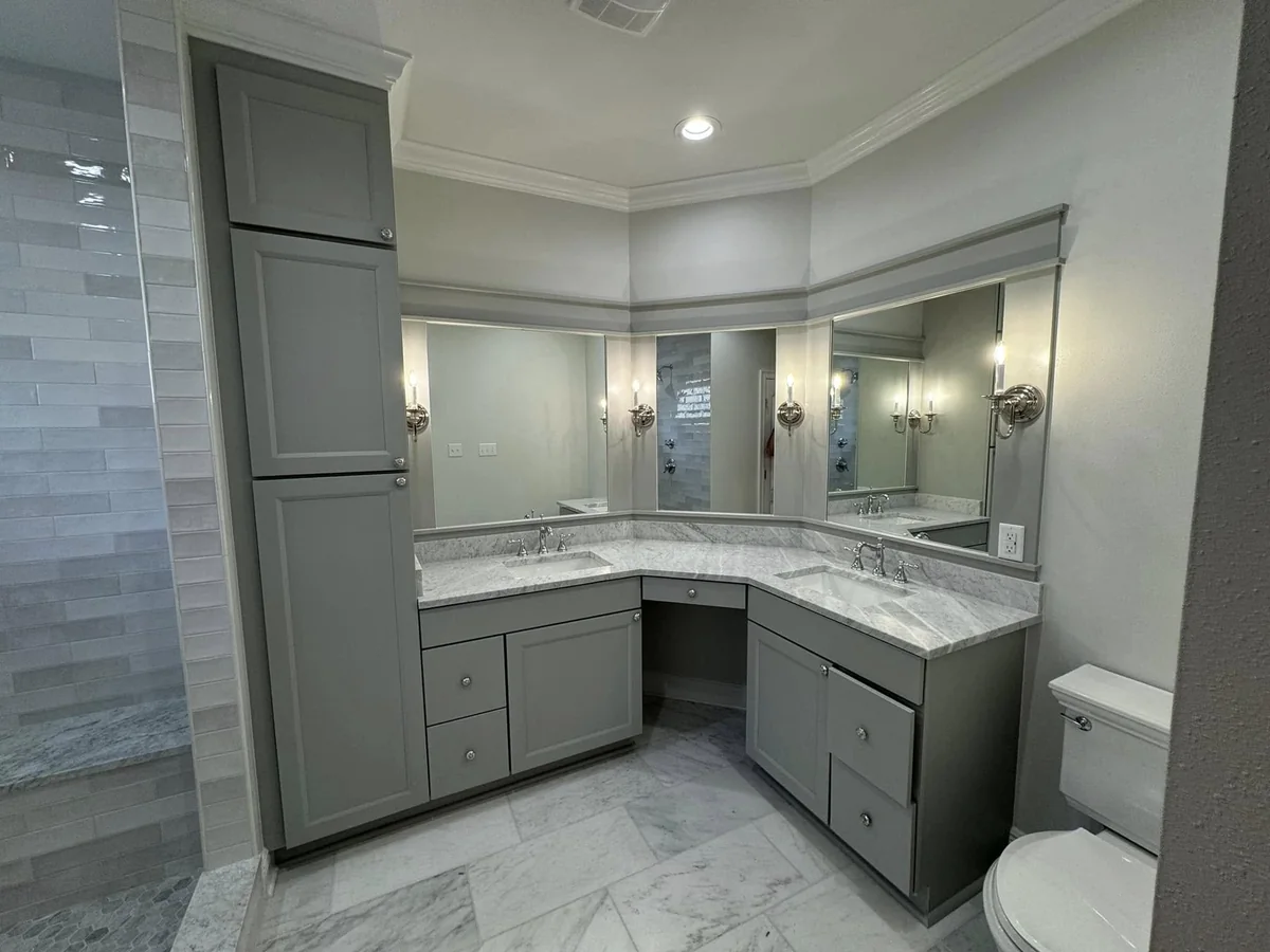 Bathroom corner vanity with gray cabinetry and light stone countertops
