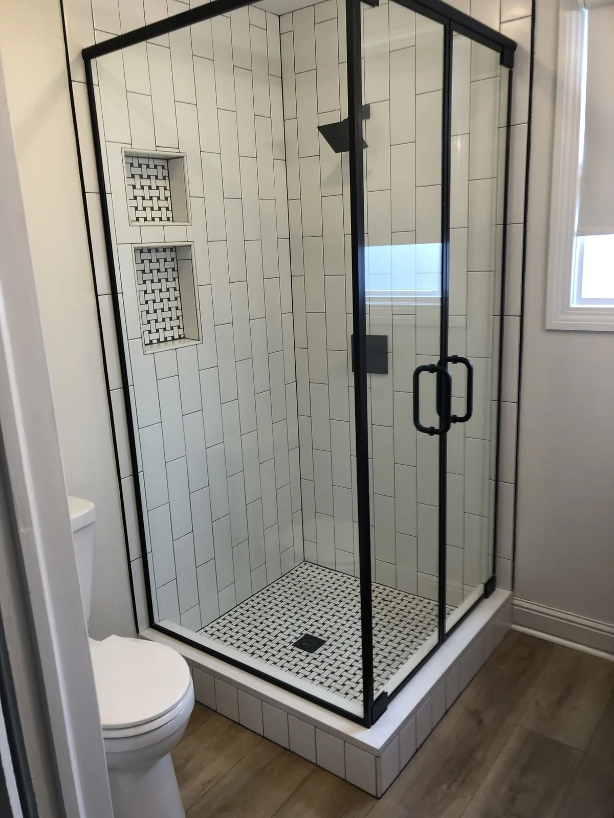 Glass shower with black framing, vertically arranged wall tile, and recessed niches.