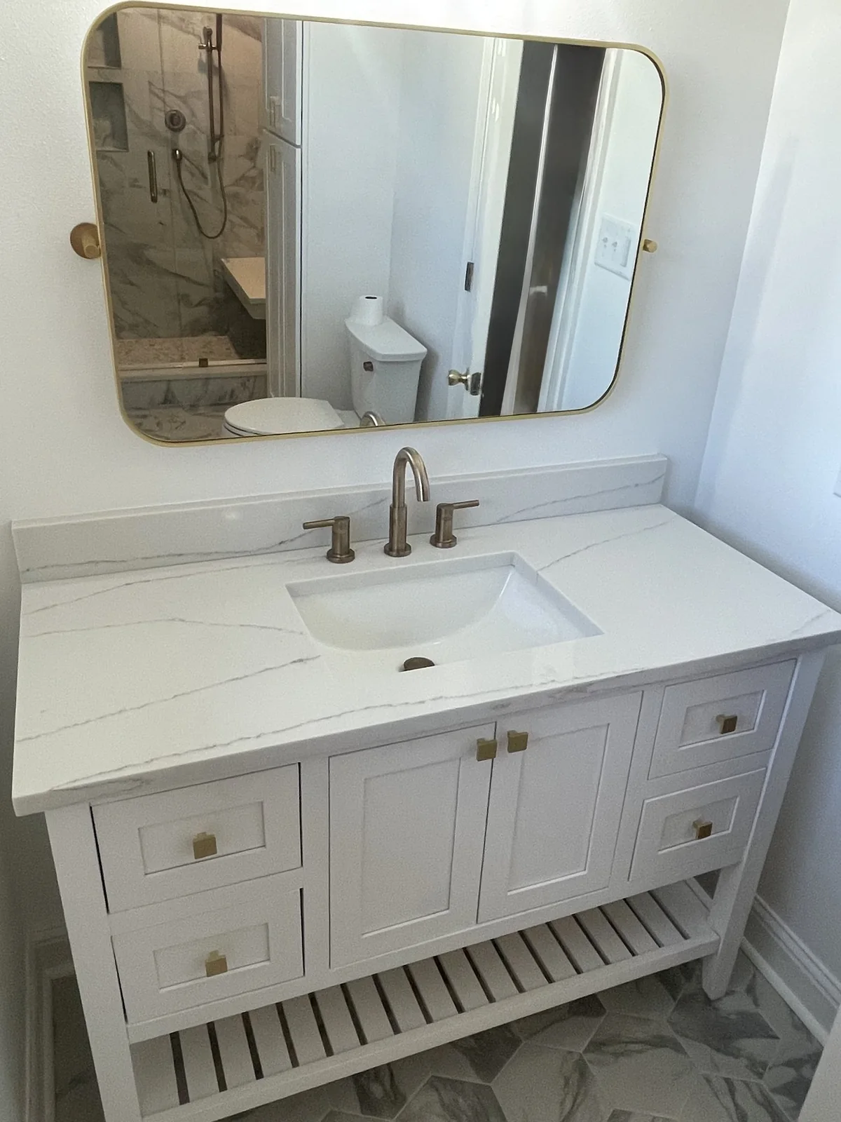 White bathroom vanity with an open lower shelf and a wide mirror.
