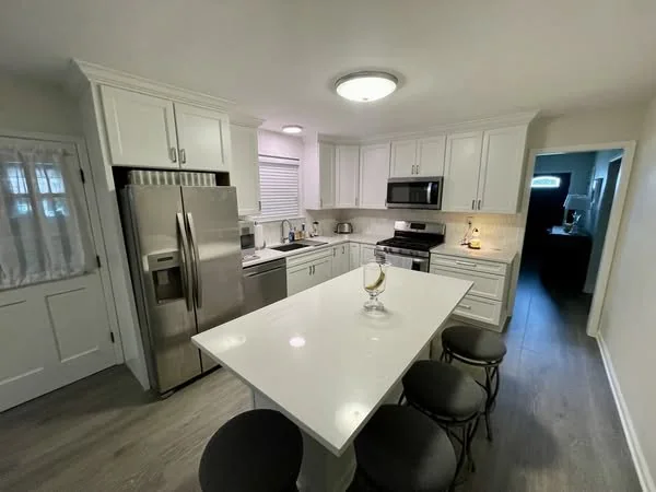 White kitchen with a stone island and stainless steel refrigerator