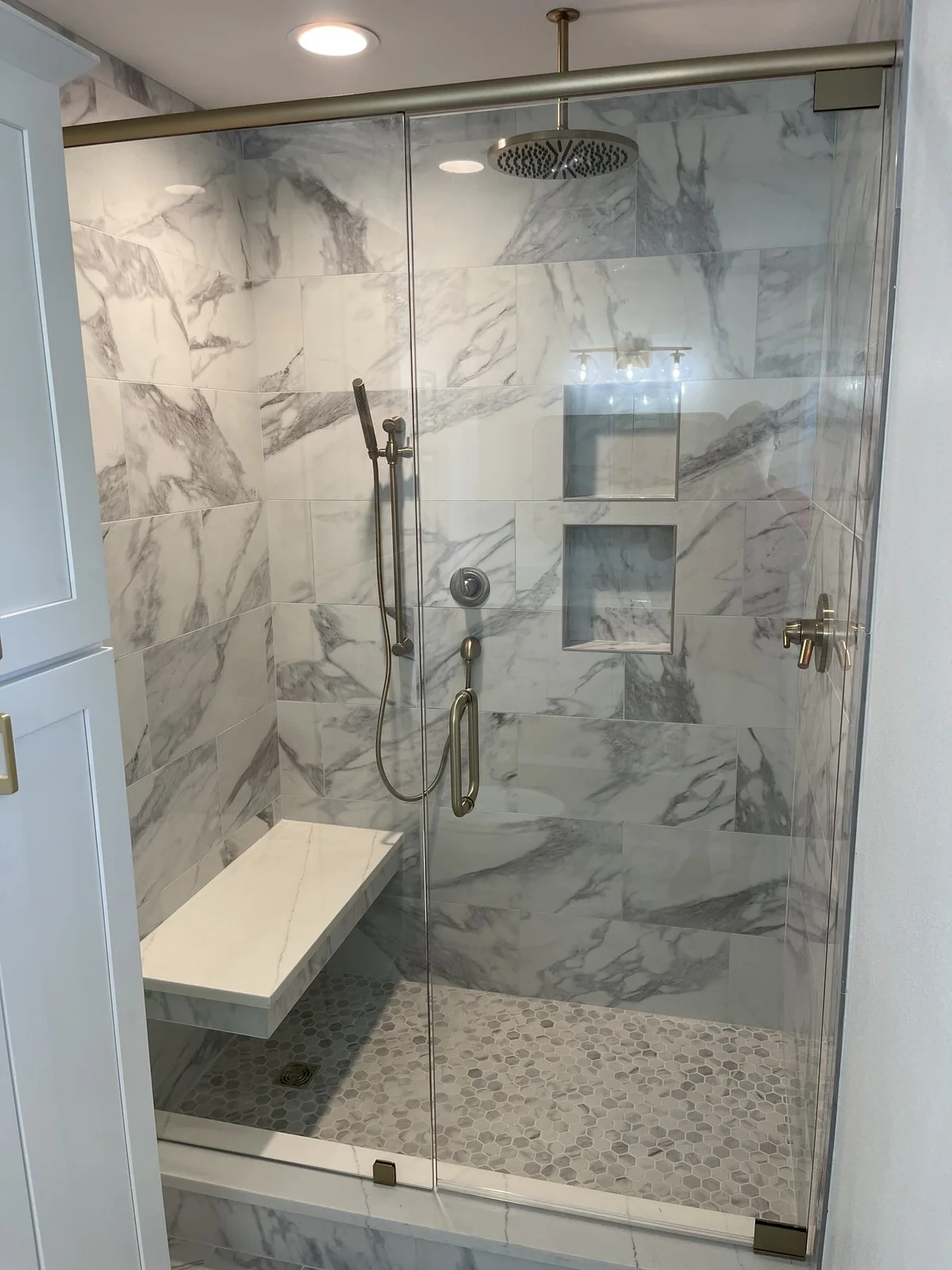 Glass-enclosed shower with a bench, recessed niches, and patterned tile.