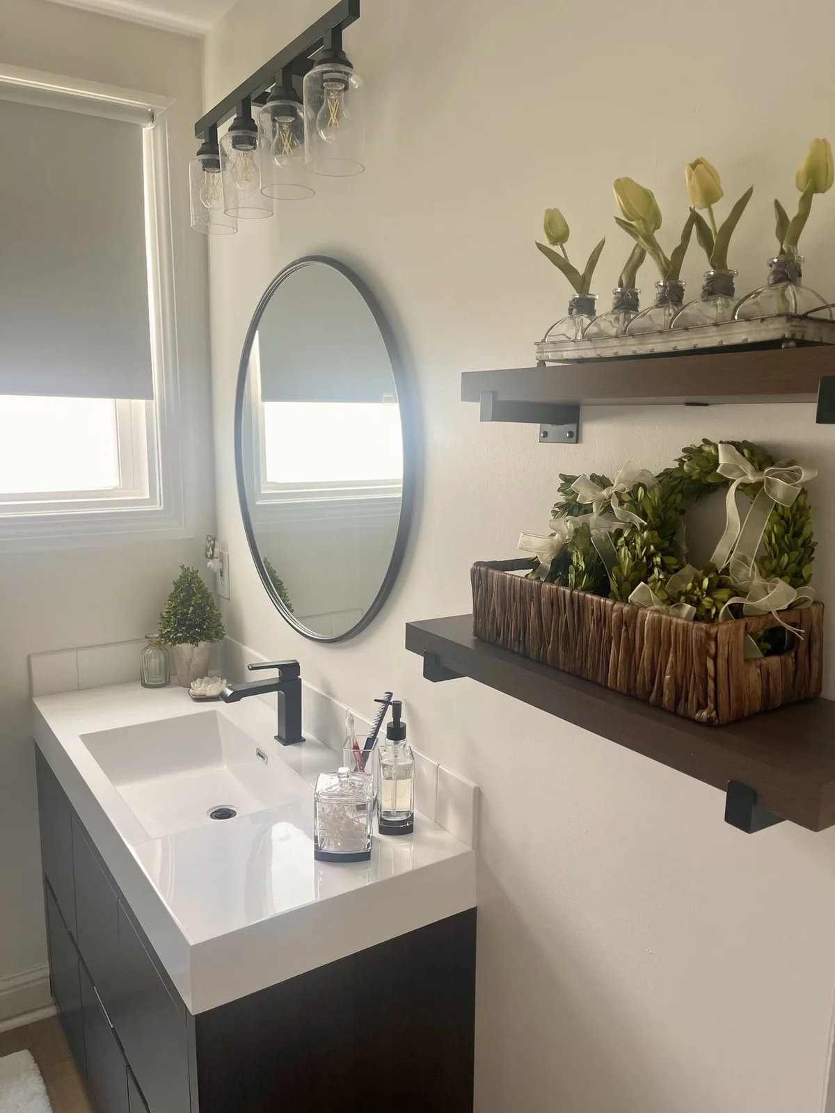 White basin and countertop with a black faucet beneath a round mirror.