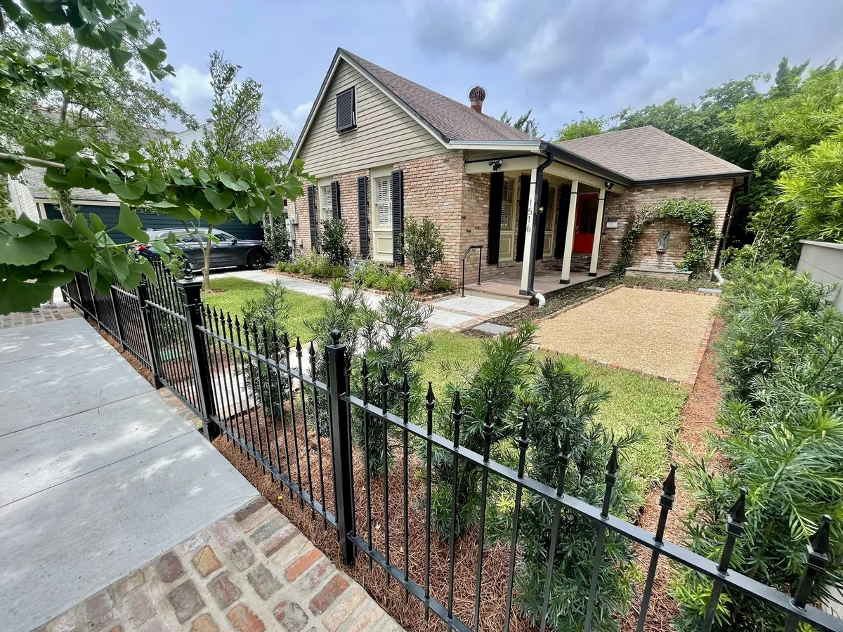 Brick home with a front porch, landscaping and black iron fence