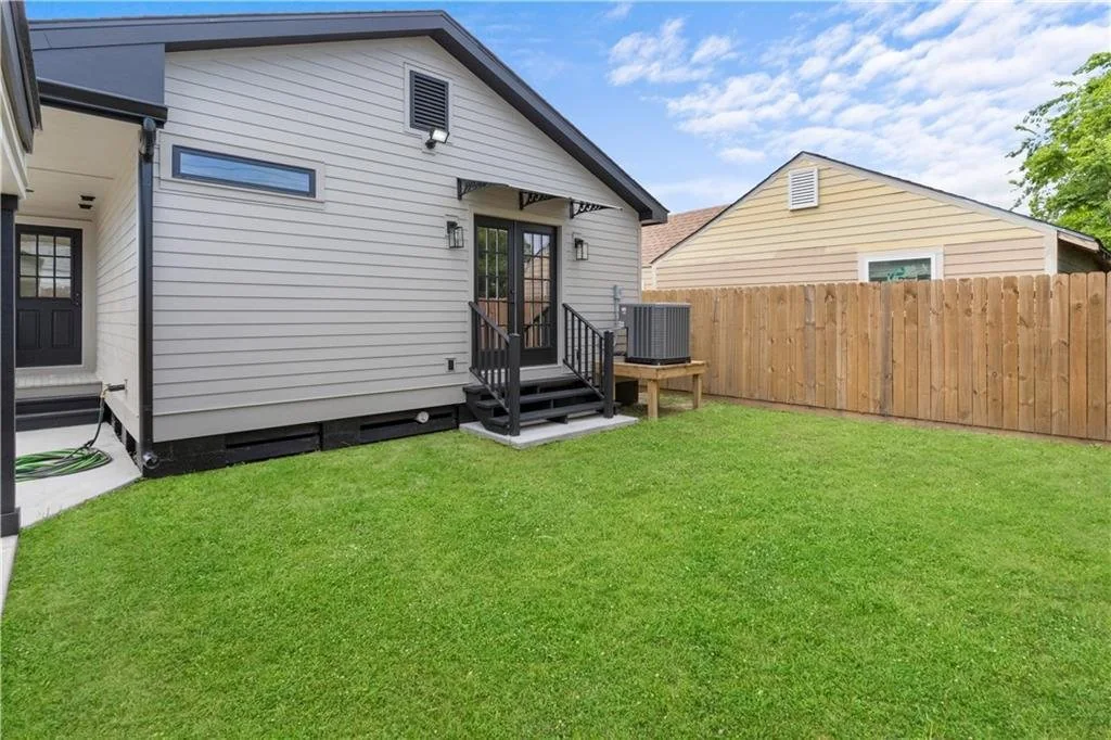 Rear exterior of a renovated home with light siding, French doors, steps and a fenced lawn.