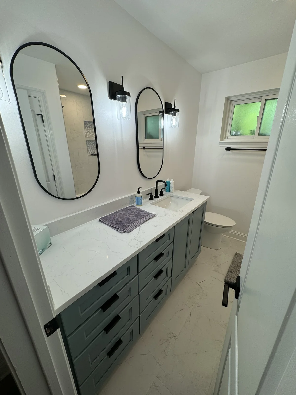 Gray double vanity with black fixtures and oval mirrors