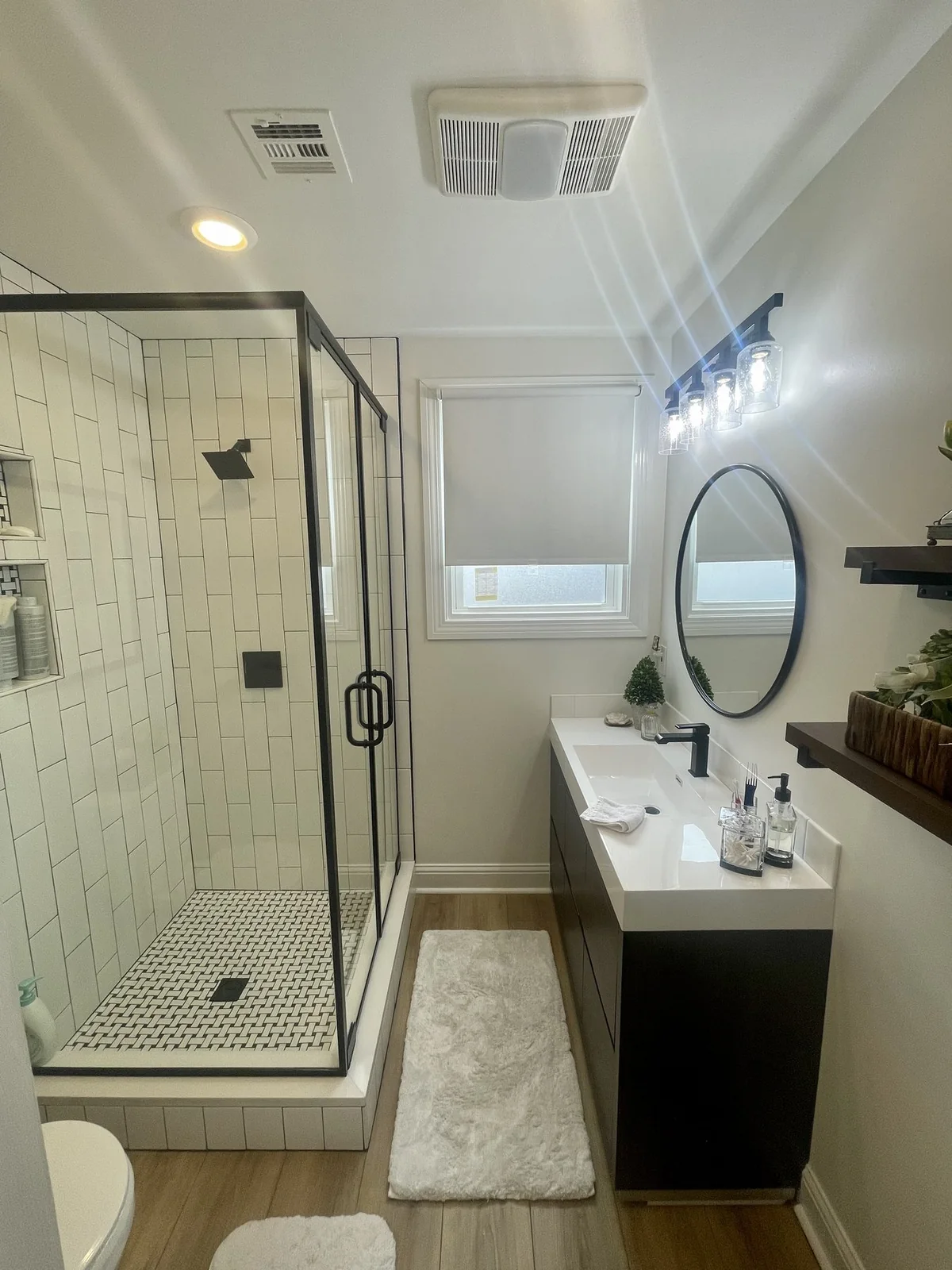 Completed bathroom with a glass shower, dark vanity, round mirror, and black fixtures.